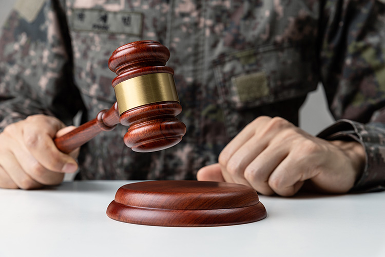 Hand of soldier holding gavel at courtroom.